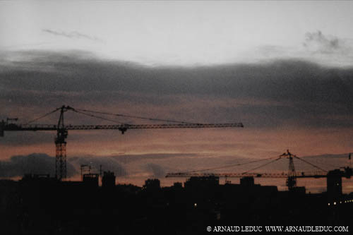 paysage urbain de sihhouettes d'immeubles et de 2 grues de construction au coucher du soleil, ciel nuageux rougeoyant